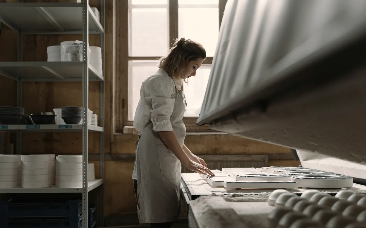 Worker in a ceramics workshop next to shelves of tableware